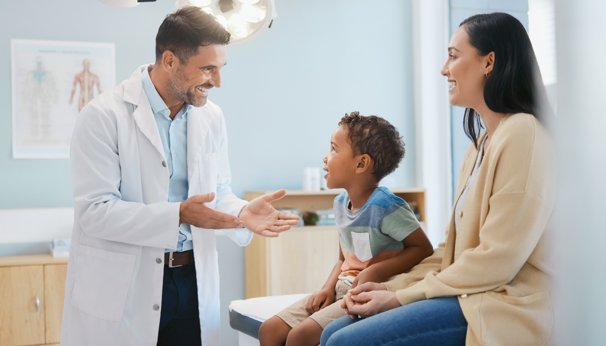 Doctor smiling and talking to a child and woman in a medical exam room.