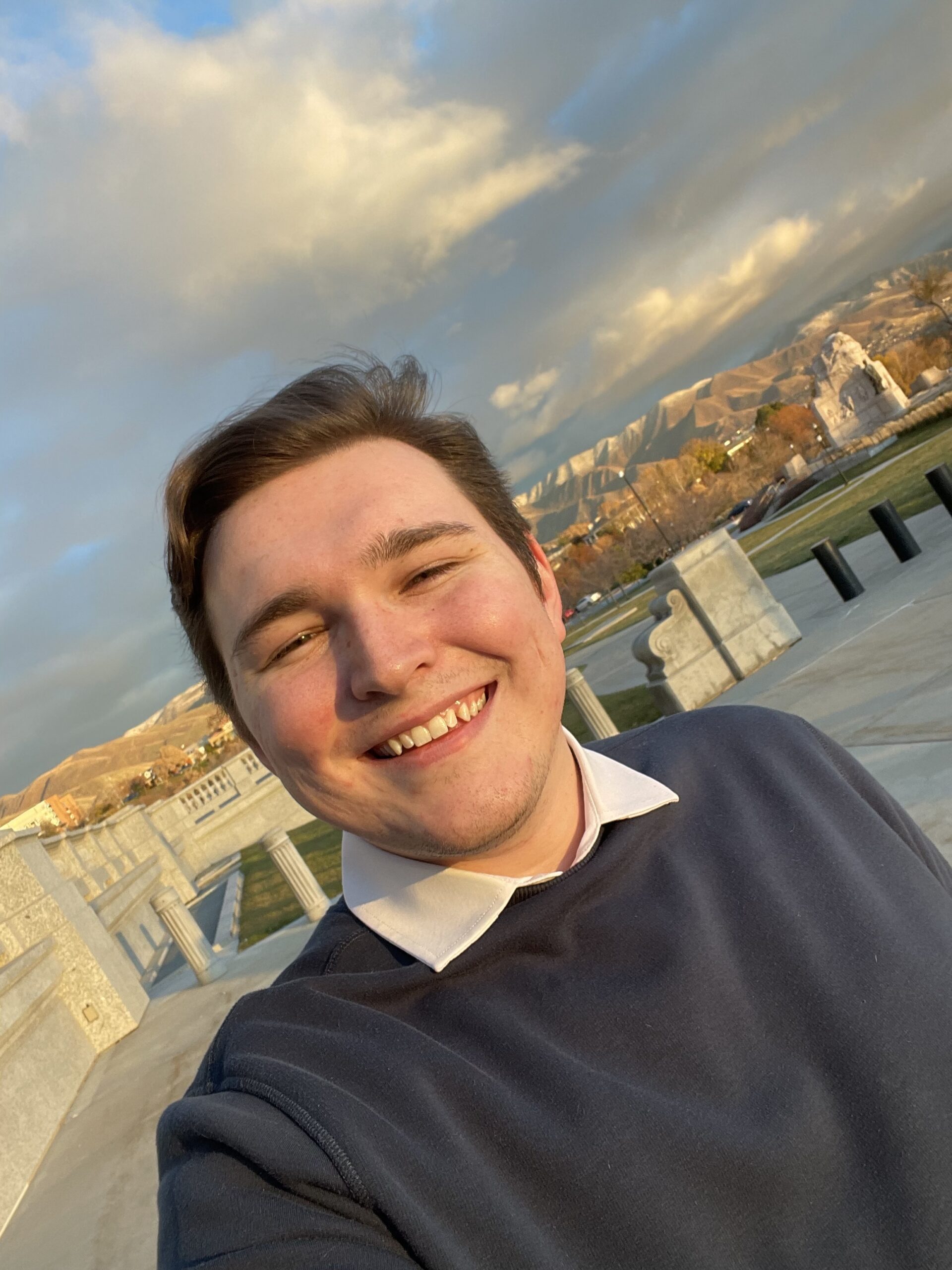 Justice Burt smiling outdoors with mountains, blue sky, and stone structures in the background.